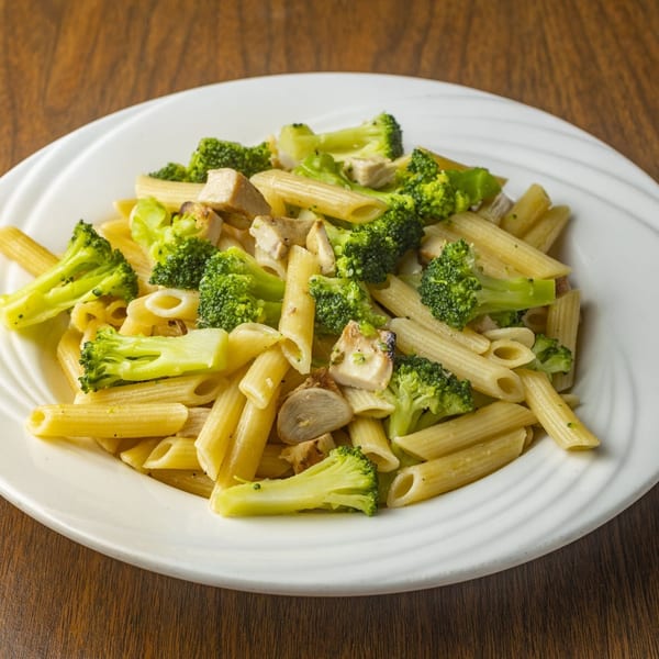 Penne pasta with chicken and broccoli florets on a white plate, on a wooden table.