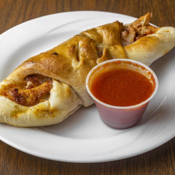 Golden-brown calzone filled with chicken and cheese, served with a side of marinara sauce.