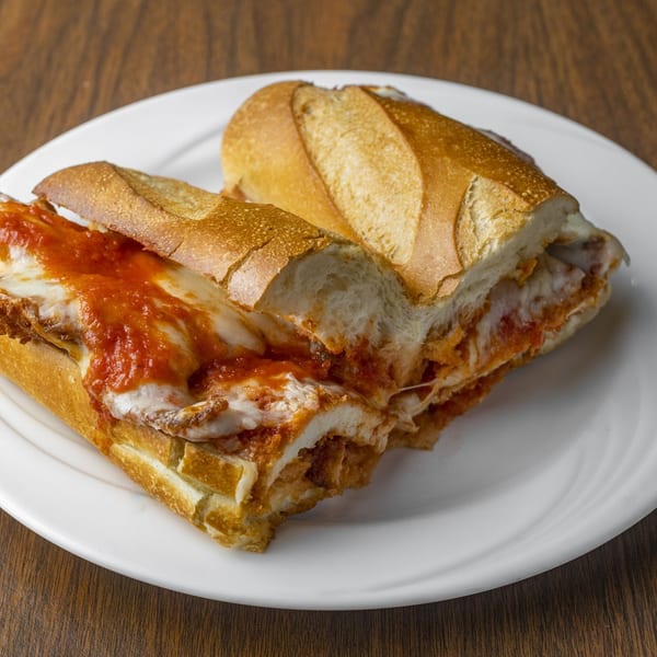A chicken parmesan hero sandwich, cut in half, on a white plate on a wooden table.