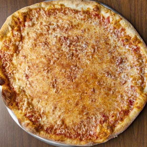 A large, round cheese pizza with a golden crust sits on a wooden table.