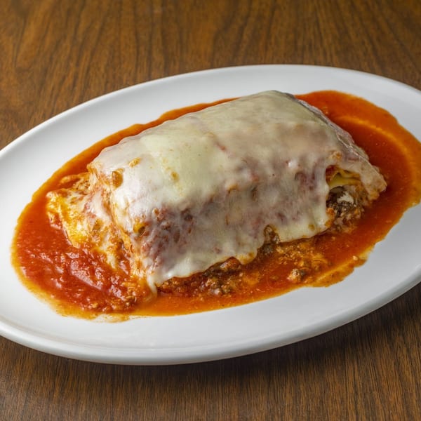 A large serving of lasagna with melted cheese and red sauce on a white oval plate.